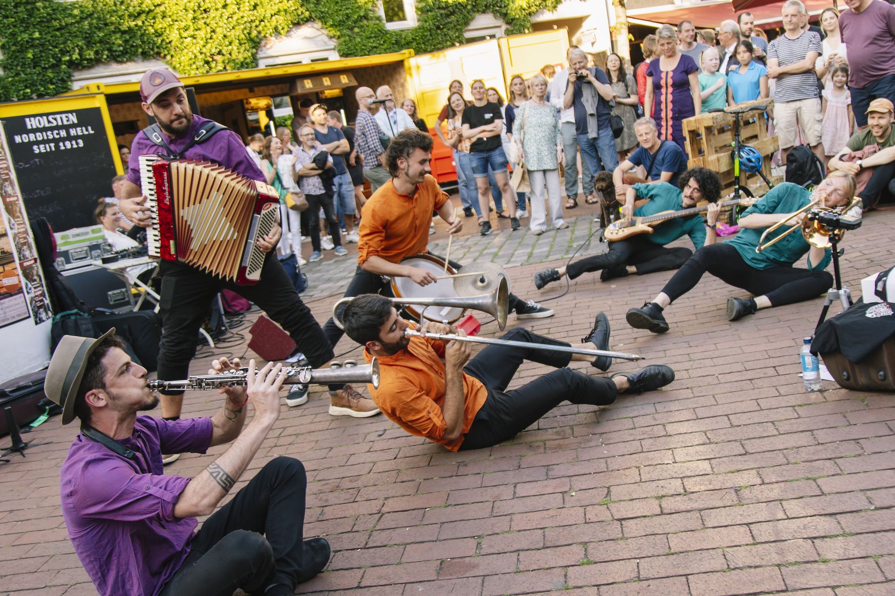 Desmadre Callejero tocando en la calle, con músicos en el piso y el público alrededor